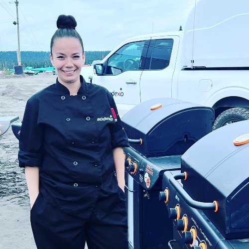 Woman in chef's coat outdoors with BBQs 